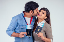 Happy Indian Couple Holding Passport Of India With Airline Tickets Inside In Studio White Background And Kissing At Cheek