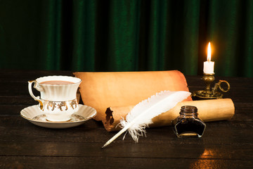 Wall Mural - A cup of drink, a scroll of papyrus, a feather, and a candle in a candlestick against the background of green curtains