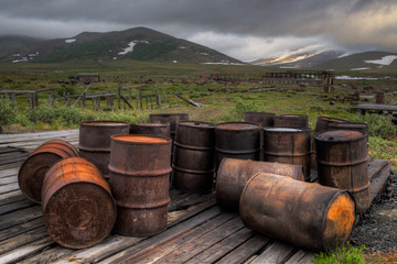 Wall Mural - Rusty barrels and ruins of an abandoned village of gold miners. Dramatic landscape with industrial trash in a mountain valley. Problems of ecology and nature pollution in the Arctic. Chukotka, Russia.
