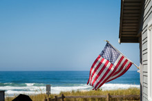 A Beautiful Oceanfront Property With A Classic American Flag On The Side Of It With The Coastline In The Background.
