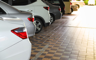 Closeup of rear side of white car with  other cars parking in indoor parking area with bright sunlight. 