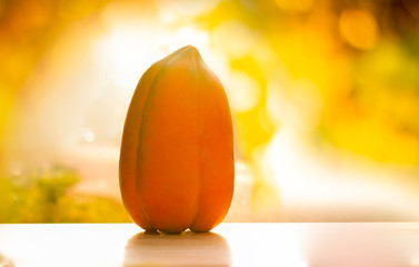 Ripe papaya, yellow skin, appetizing, placed on a wooden table with a light orange background, orange morning.