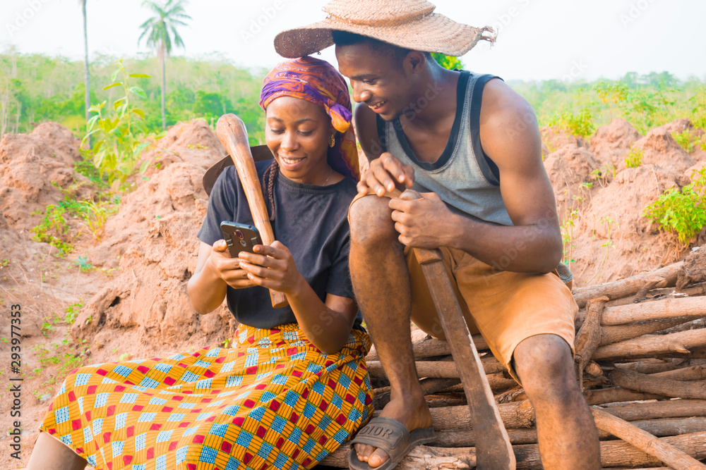 excited african couple doing internet banking on their farmland. male and female farmers using smartphone