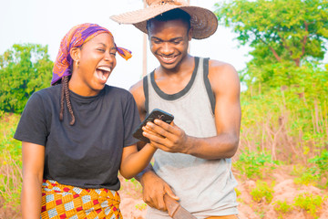 excited african couple doing internet banking on their farmland. male and female farmers using smartphone