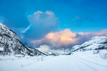 Wall Mural - arctic ice road covered in snow leads to a valley between hills at sunset