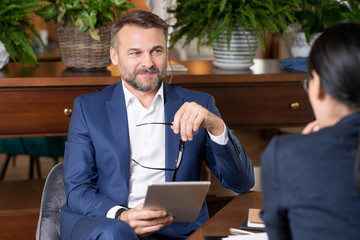Poster - Successful elegant businessman with touchpad and eyeglasses talking to colleague