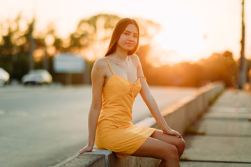 Wall Mural - A woman sits on the sidewalk on a background of cityscape at sunset.