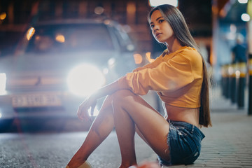 Wall Mural - A woman sits on sidewalk against background of night city.