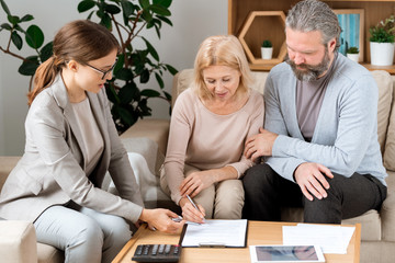 Canvas Print - Young agent pointing at place for signature while mature client signing document