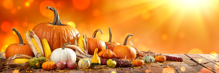 Wall Mural - wooden harvest table with pumpkins corncobs gourds and apples with orange bokeh and sunlight backgro