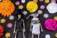 Flat Lay With Groom And Bride Skeletons And Colorful Flowers On Black Background, Day Of The Dead Decoration