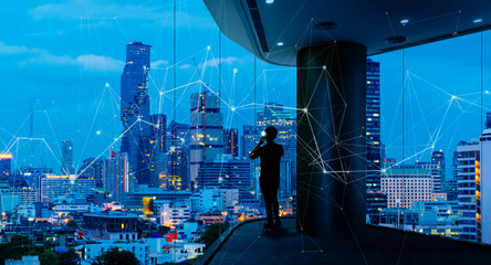Fototapete - Businessman standing using smart phone in modern space watching city night view.Business with ambition and vision concept.and wireless network low poly line.