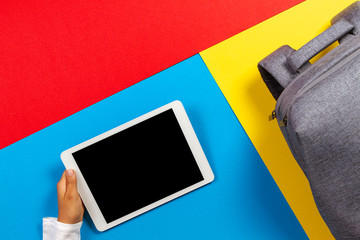 Wall Mural - Top view to kid hands with tablet computer and gray backpack on colorful background