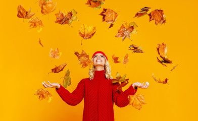 happy emotional cheerful girl laughing  with autumn leaves and knitted autumn red cap  on colored yellow background.