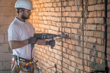 Handyman uses jackhammer, for installation, professional worker on the construction site. The concept of electrician and handyman.