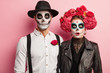 © WHstudio Leushin N - Loving couple in costumes of skeletons and skull makeup, have scared expressions, celebrate autumn holiday, pose during horror party, isolated over pink background. Happy Halloween time concept