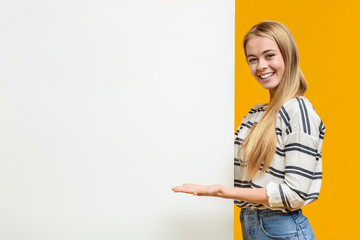 Beautiful girl pointing at white blank placard with open palm