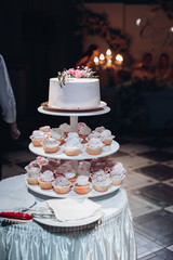 Wall Mural - Front view of beautiful wedding cake with flowers staying on table. Delicious dessert for celebration. Lovely pair at background. Concept of love, confectionery and biscuit.