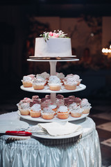 Sticker - Front view of beautiful wedding cake with flowers staying on table. Delicious dessert for celebration. Lovely pair at background. Concept of love, confectionery and biscuit.