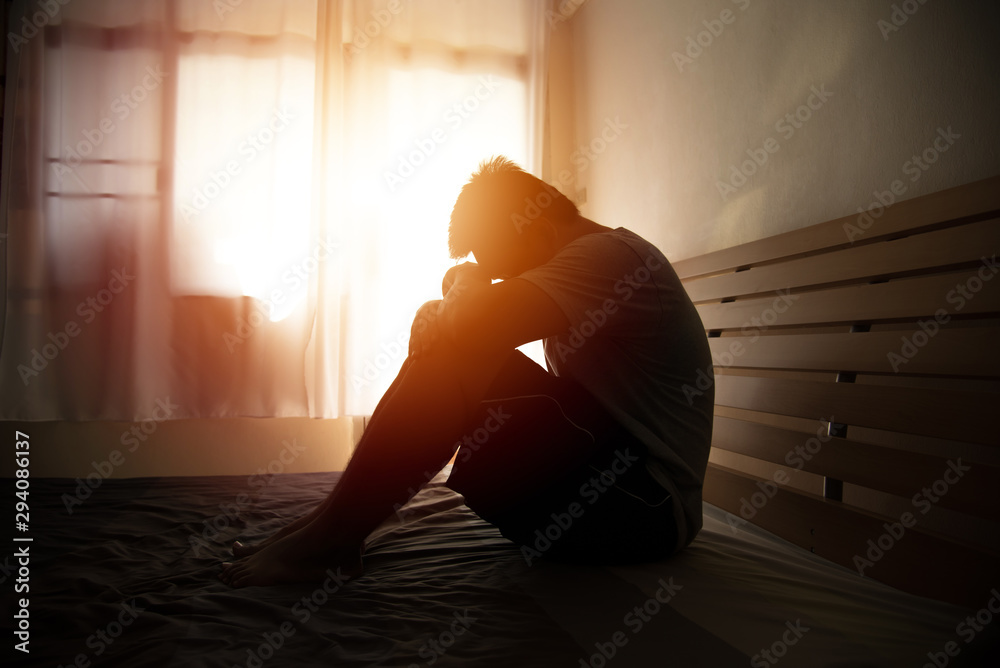 desperate man in silhouette sitting on the bed with hands on head - obrazy, fototapety, plakaty 