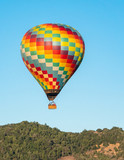 A colorful hot air balloon flies high in the sky early in the morning at sunrise above the Napa Valley, California, known for its vineyards and wineries in addition to ballooning.  