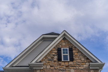 Wall Mural - Double gable with colored stone facade siding, double hung window with white frame, vinyl shutters on a pitched roof attic at a luxury American single family home neighborhood USA