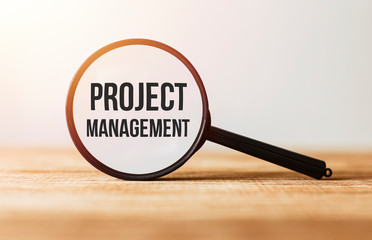 Poster - magnifying glass with text project management on wooden table.