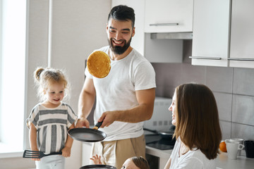 bearded happy father showing tricks with pancakes in the kitchen, close up photo.