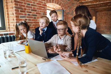 Wall Mural - blonde boy in glasses and his friends sitting in front laptop and making up a plan for prosperous business