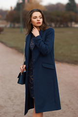 Pretty beautiful yong woman walking in park on a windy autumn day. Lady in blue coat with handbag. Fashion look