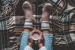 Leinwandbild Motiv Cozy woman in knitted winter warm socks and in pajamas holding a cup of hot cocoa during resting on checkered plaid blanket at home in winter time. Cozy time and winter drinks. Top view