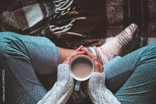 Cozy woman in knitted winter warm socks and in pajamas holding a cup of hot cocoa during resting on checkered plaid blanket at home in winter time Tableau sur Toile