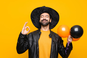 Wall Mural - Man with witch hat holding black and orange air balloons for halloween party in zen pose