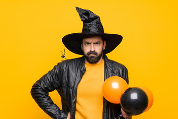 Wall Mural - Man with witch hat holding black and orange air balloons for halloween party angry