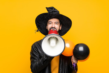 Wall Mural - Man with witch hat holding black and orange air balloons for halloween party shouting through a megaphone