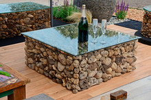 A Modern Looking Glass Topped Coffee Table With A Decorative Base Made Of Driftwood Complete With Glasses And Champagne
