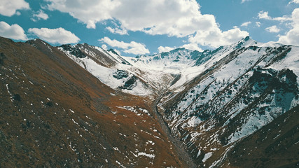 Wall Mural - Autumn in the mountains. Yellow grass and snow-capped mountains. The gorge with the river. Blue sky and big white clouds. The stones lie on the slopes, in some places the snow. Almaty, Kazakhstan.