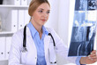 © rogerphoto - Doctor woman examining x-ray picture near window in hospital. Surgeon or orthopedist at work. Medicine and healthcare concept. Blue colored blouse of a therapist looks good