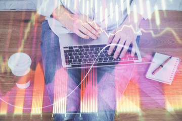 Double exposure of businessman's hands with laptop and stock market graph background. Concept of research and trading.