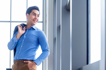 Handsome young businessman Asian caucasian wear a Long sleeve shirt and put the suit on his shoulder, be a smile and standing smart poses in a modern office.