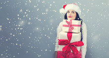 Young Woman With Santa Hat Holding Gift Boxes On A Gray Background