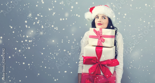 Cuadros en Lienzo Young woman with santa hat holding gift boxes on a gray background