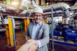© Dusan Petkovic - Handsome caucasian manager in suit and with helmet on head holding folder with documents and shaking hands with investor while standing in power plant.