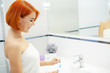 © Maksymiv Iurii - Skin care. Woman with red hair make makeup in the light bathroom.