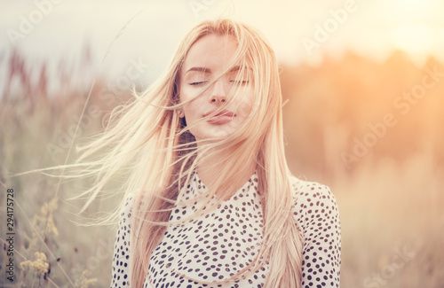 Close Up Portrait of beauty girl with fluttering white hair enjoying nature outdoors, on a field. Flying blonde hair on the wind. Breeze playing with girl\'s hair. Beautiful young woman face closeup.