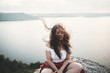 Travel and Meditation. Hipster girl with windy hair sitting and meditating on top of rock mountain with beautiful view on river. Atmospheric calm moment. Copy space
