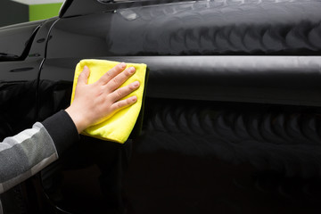 Hand polishes and waxes the black car with yellow towel for shiny look , car wash and hand wash concept