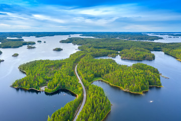 Canvas Print - Aerial view of road between green summer forest and blue lake in Finland