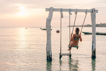 Wall Mural - Girl relaxing in swings on sunset beach