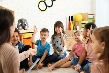 Sticker - Kindergarten teacher reading book to cute little children indoors